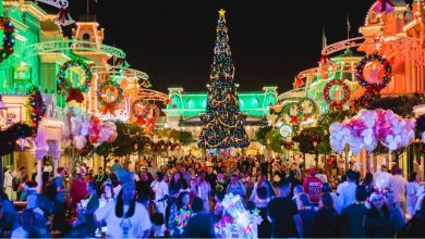 Main Street in Disney World lit up with Christmas lights and a massive tree with crowds passing by