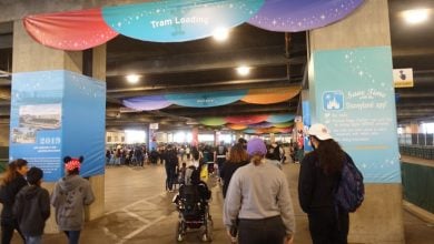Guests head to the Disneyland tram boarding area, surrounded by vibrant banners in the parking structure.