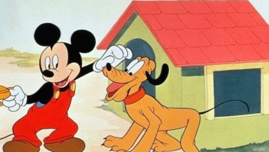 Mickey Mouse in red overalls greets Pluto beside his yellow doghouse