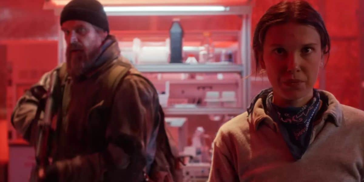 A young woman greets a visitor in a Stranger Things-themed lab, glowing red with shelves of props and science gear behind them.