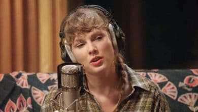 Taylor Swift wearing headphones and singing into a microphone