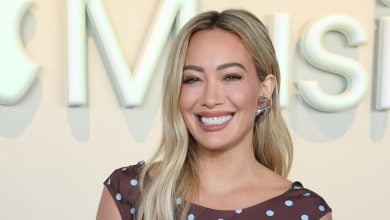 Hilary Duff beams in front of the Apple Music sign, wearing a playful polka-dot dress, ready to shine for awaiting fans.