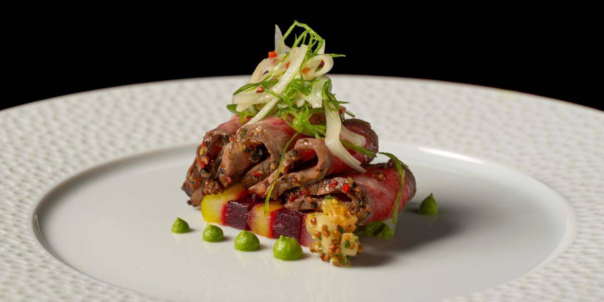 Gourmet dish at Disneyland Resort with sliced meat, veggies, green sauce dots, and herbs—perfect for Disney food lovers.