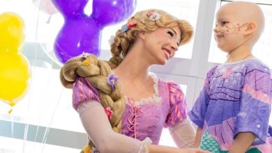 Belle from Beauty and the Beast chats with a young fan in a hospital hallway, surrounded by festive balloons.