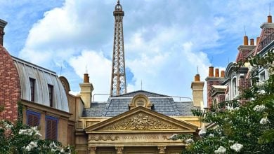 The Eiffel Tower stands behind elegant Parisian facades and flowering trees, creating a scene reminiscent of EPCOT’s France Pavilion.