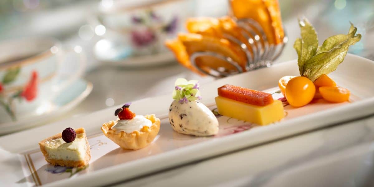 A magical dessert plate at Disney's Main Street Bakery, featuring whimsical pastries, fresh fruit, cream, and teacups nearby.