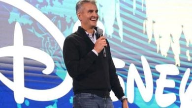 Josh D'Amaro on stage with "Disney" written in bright white letters on the screen behind him