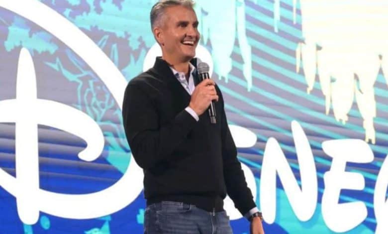 Josh D'Amaro on stage with "Disney" written in bright white letters on the screen behind him
