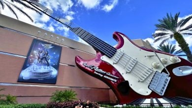 The giant red guitar marks the entrance to Rock 'n' Roller Coaster at Disney's Hollywood Studios, surrounded by palm trees and a mural.