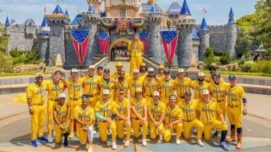 A baseball team in bright yellow uniforms smiles for a group photo in front of Cinderella Castle at Disney World.