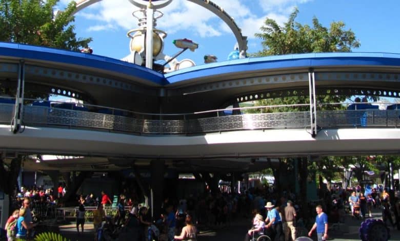 Guests stroll beneath the iconic PeopleMover track in Tomorrowland at Magic Kingdom