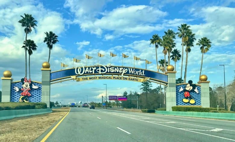 Walt Disney World entrance arch with Mickey and Minnie, palm trees, blue sky, and excited families arriving in Orlando traffic. Florida Cyclospora outbreak Disney World