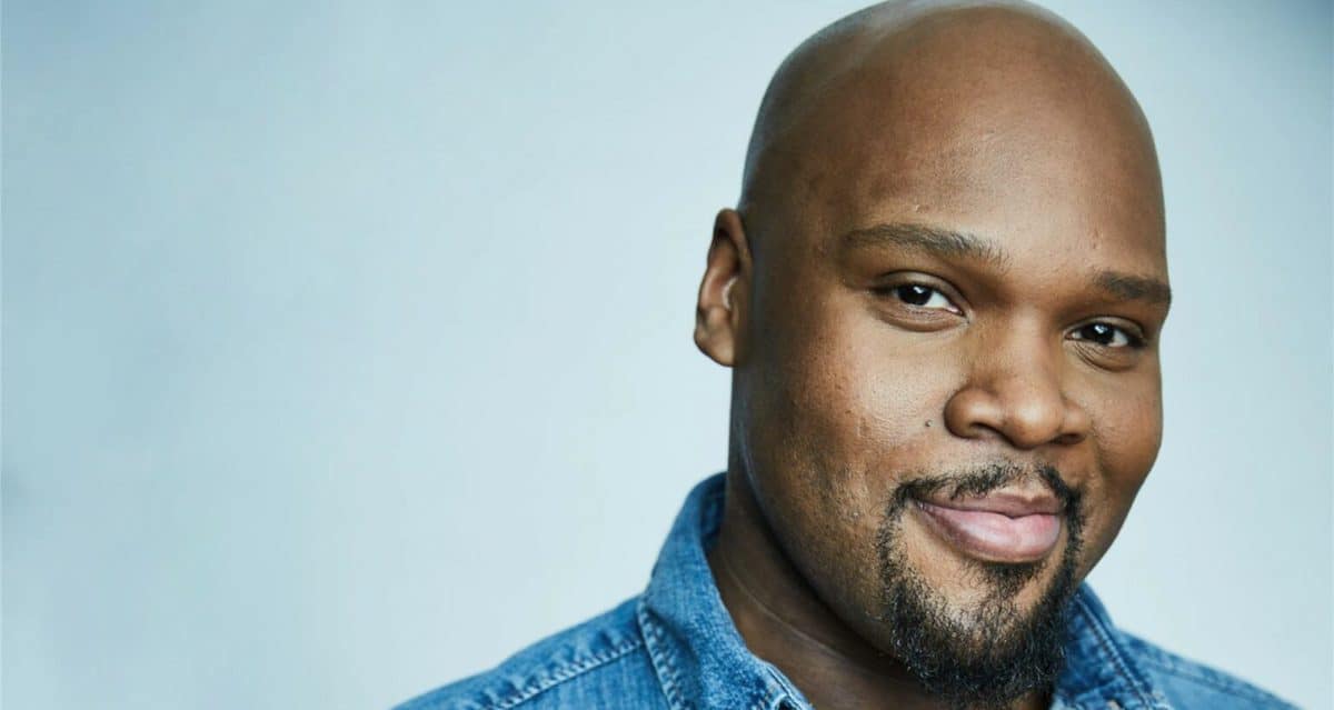 A smiling guest with a shaved head and goatee in a blue denim shirt, lit by magical Genie vibes, ready for his Disney farewell.