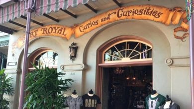 Entrance to Curios and Curiosities, styled like a whimsical theme park shop, with costume displays and lush plants by the awning.
