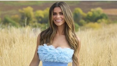 A guest in a Cinderella-inspired blue ruffled dress smiles in a golden field, creating a magical fairytale moment, trees behind her.