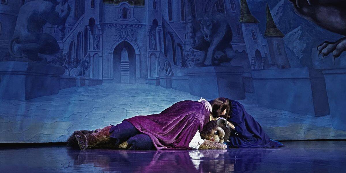 Beauty and the Beast perform on stage, kneeling before a magical blue castle backdrop at a Disney park show.