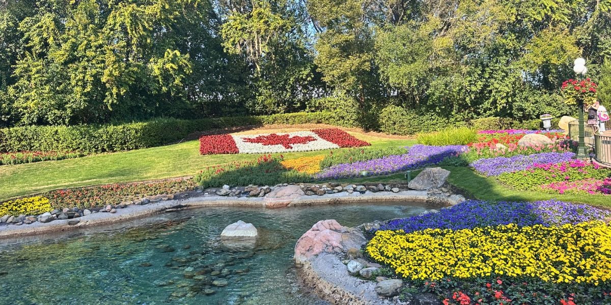 A stunning garden display with a Canadian flag flowerbed, colorful blooms, and a scenic pond, evoking Disney park magic.