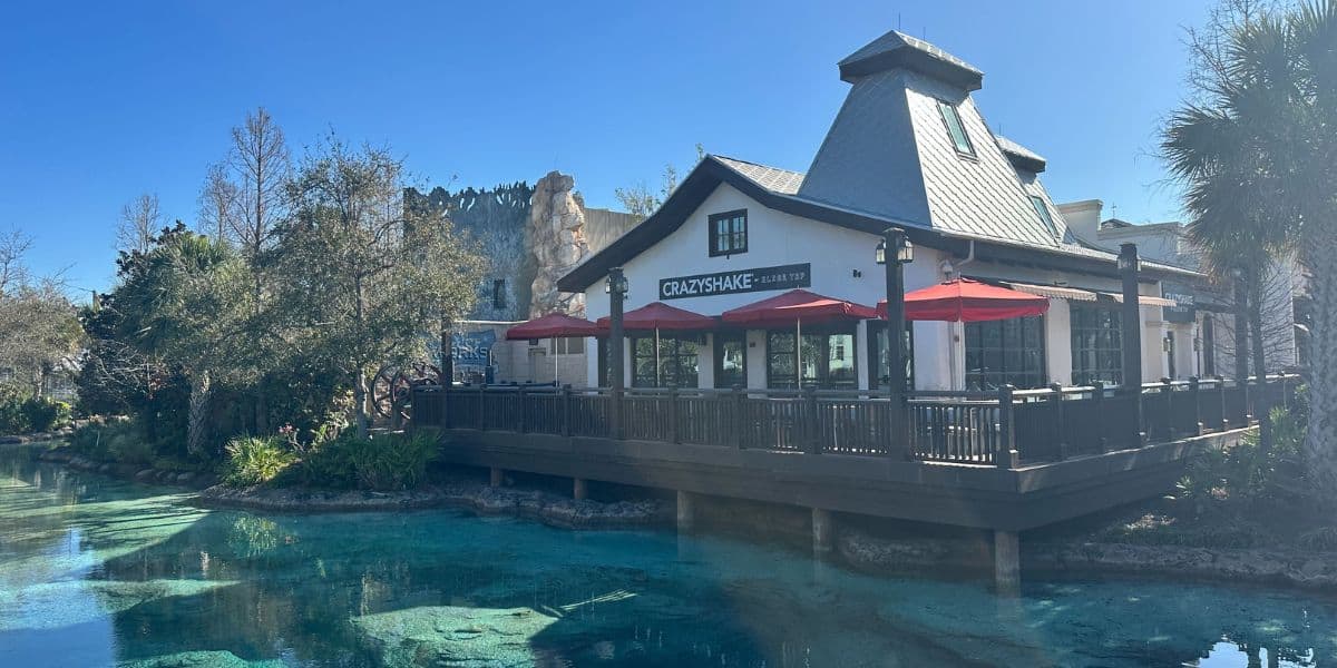 An outdoor café with vibrant red umbrellas lines the stream at Epcot, shining under a bright sunny sky.