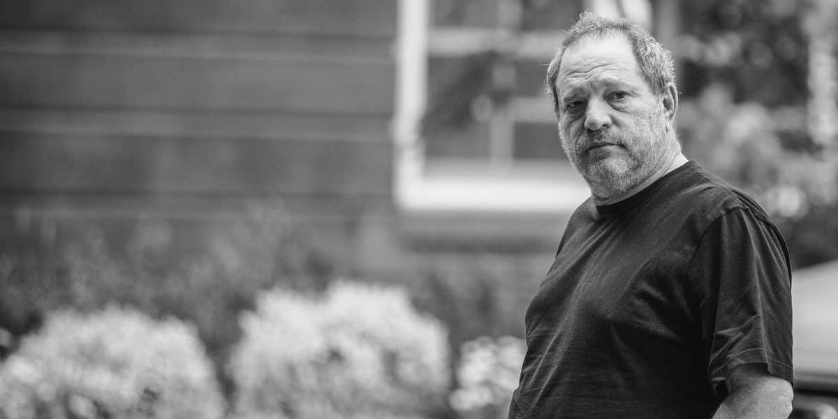 A bearded man in a dark shirt stands outside with blurred greenery, recalling headlines about Weinstein’s Disney pension.