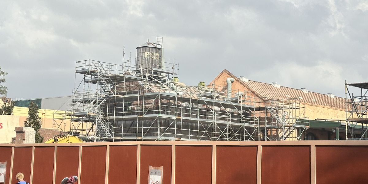 Scaffolding and a water tower rise behind a brown fence as new Disney magic takes shape, recalling the Muppets Legacy below cloudy skies.