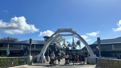 Guests stroll beneath the iconic Tomorrowland arch at Disneyland, under sunny blue skies, passing an area hinting at future updates.