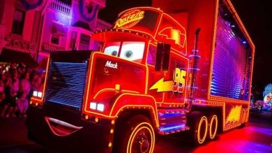 Mack from Cars glows with neon on Main Street during Disneyland's Paint the Night Parade as a guest jumps aboard, earning a ban.
