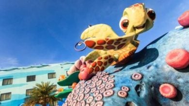 Vibrant turtle statue on coral outside a blue resort building with palm trees, evoking Disney-inspired fun for park guests.