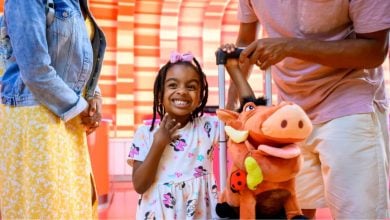 young guest with suitcase and Pumba stuffed animal waits in disney's hotel lobby with her parents