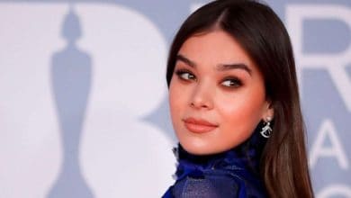 Performer in a vibrant blue costume poses before a lively, lettered backdrop at an entertainment event or theme park.