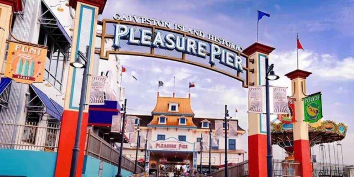Galveston Island Historic Pleasure Pier entrance with vibrant signs and thrill rides, including the roller coaster in back.