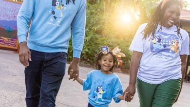 Smiling family in Disney shirts stroll hand-in-hand under the sun at Animal Kingdom, soaking up the magic of Disney.