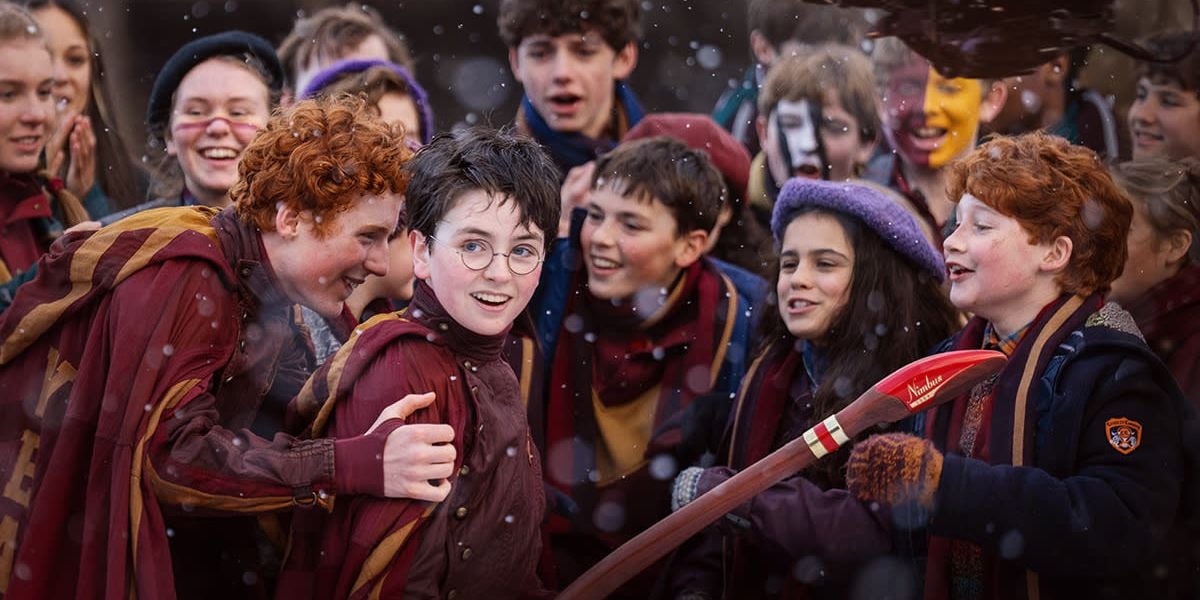 Kids bundled up for a snowy holiday festival cheer outside as one waves a bright red broomstick, winter magic all around.