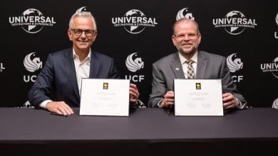 Universal and UCF executives sign partnership documents at a branded table, celebrating collaboration in themed entertainment.