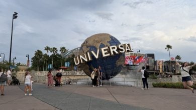 Visitors strike playful poses by the iconic Universal globe as someone leaps with excitement on the right side of Universal Studios.