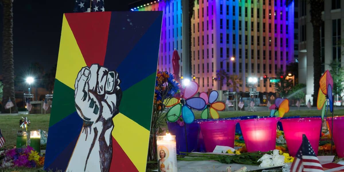 A vibrant painting of a raised fist on a rainbow backdrop shines at a candlelit vigil tribute, commemorating Pulse victims.