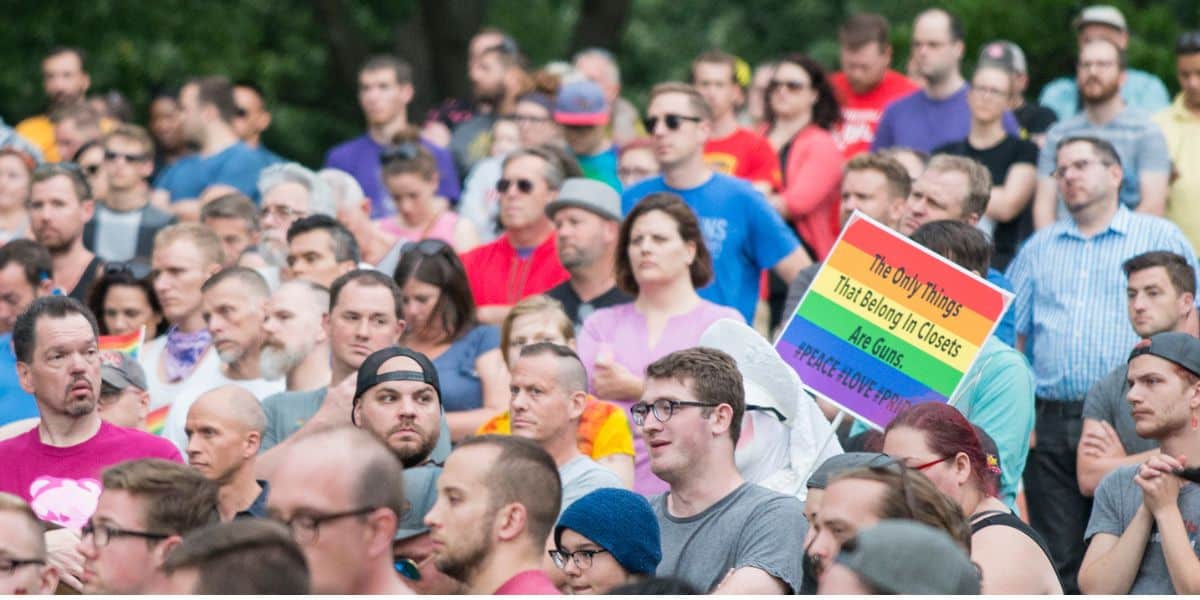 A vibrant rally audience, rainbow sign referencing guns and closets, Pulse tragedy, and urging for police presence.