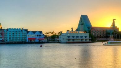 Disney’s BoardWalk at sunset, with dance hall, resort hotels, and a boat along the lively waterfront entertainment district.
