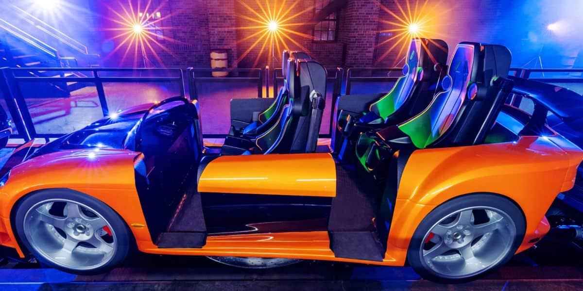 Vibrant orange coaster car with four seats, glowing beneath dynamic lights inside the park’s indoor thrill zone.