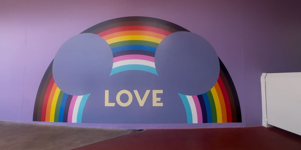 A vibrant purple wall at Disney World features a rainbow, Mickey ears, and "LOVE" in support of Pride Month and LGBTQ+ inclusivity.