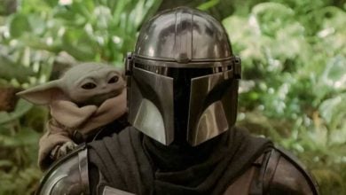 Grogu peeks behind The Mandalorian as they stand together.
