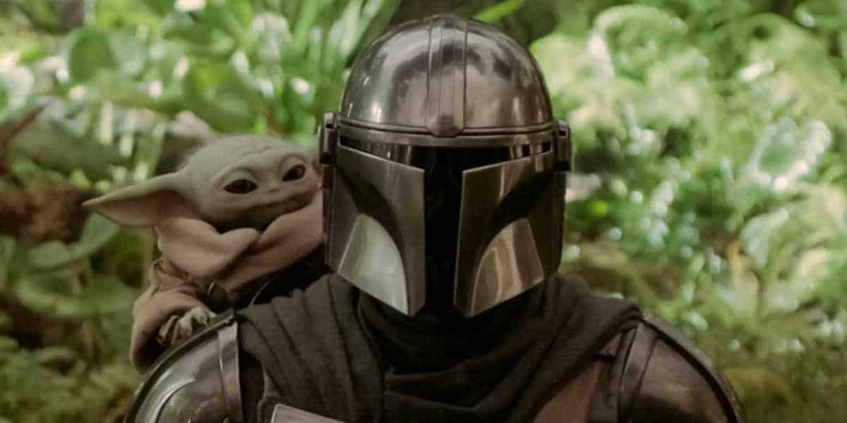 Grogu peeks behind The Mandalorian as they stand together.