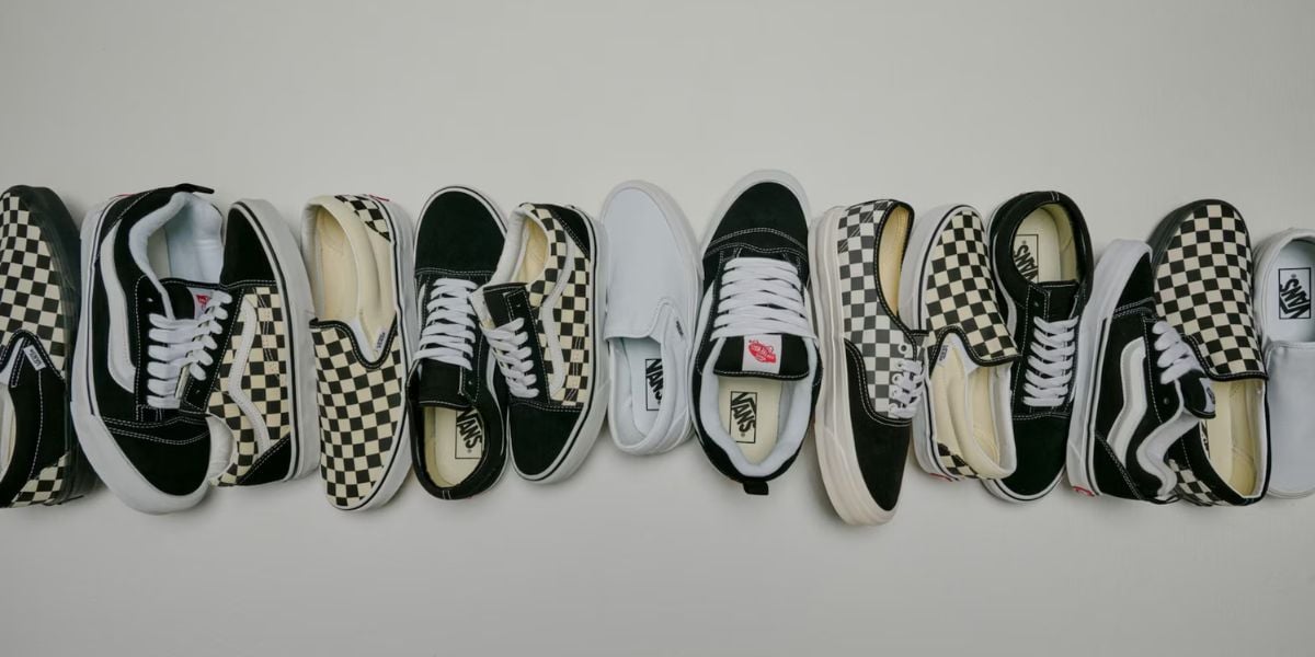 Classic Vans sneakers—black, white, and checkerboard styles—lined up like theme park icons on a crisp white stage.