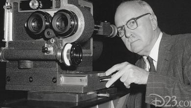 A Disney Imagineer with glasses operates a vintage film camera, peering through the viewfinder and carefully adjusting the controls—capturing the behind-the-scenes wonder that brings iconic attractions and entertainment to life, reminiscent of the movie magic created during Mary Poppins’ production.