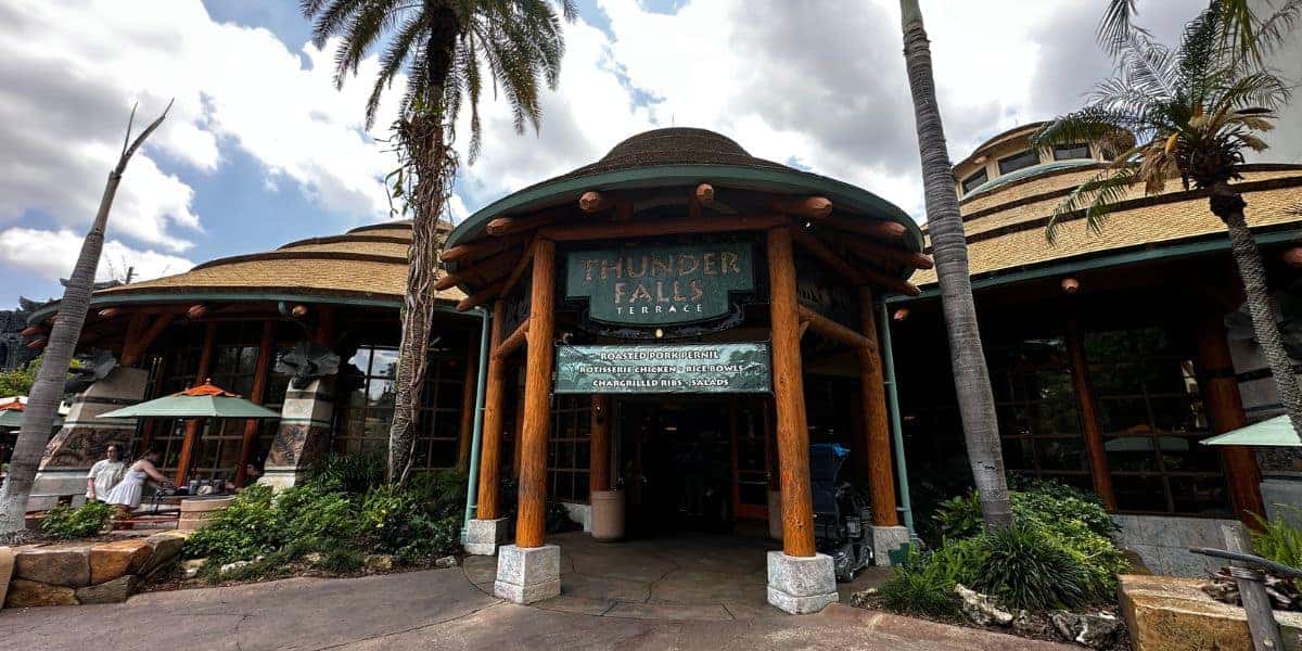 Thunder Falls Terrace at Universal’s Islands of Adventure, featuring dramatic tiki-inspired architecture, swaying palm trees, and expansive windows overlooking Jurassic Park.