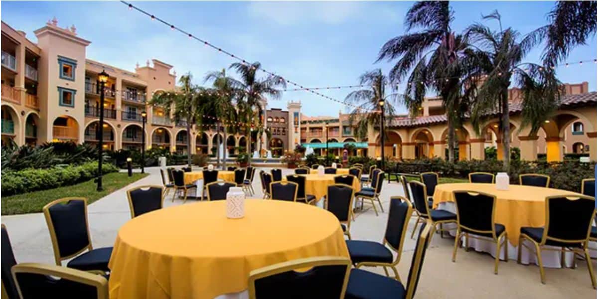 An inviting outdoor courtyard at Walt Disney World Resort, featuring round tables draped in cheerful yellow cloths, twinkling string lights overhead, and swaying palm trees—a perfect spot for guests to unwind and find comfort after the recent park closure.