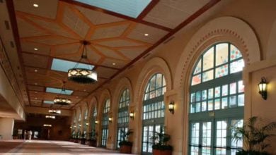 Elegant hallway at Walt Disney World featuring grand arched windows, sparkling chandeliers, lush potted plants, and ornate ceiling panels, offering a warm and welcoming space for guests during the resort closure.