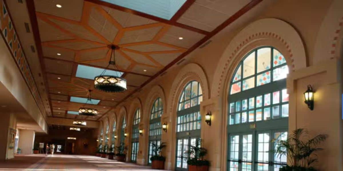 Elegant hallway at Walt Disney World featuring grand arched windows, sparkling chandeliers, lush potted plants, and ornate ceiling panels, offering a warm and welcoming space for guests during the resort closure.