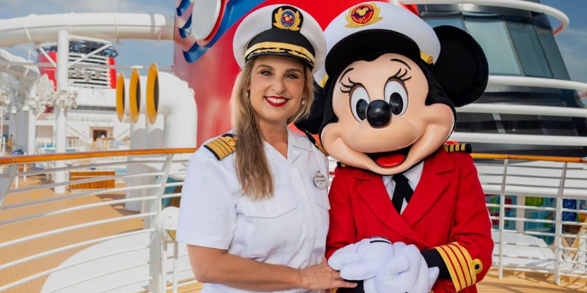 Captain Maria, the beloved Disney Cruise Line captain, poses happily with Minnie Mouse in her signature red blazer on the sunny deck of a Disney ship.
