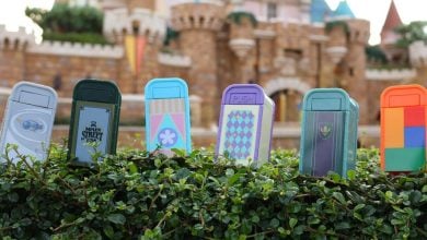 Six colorful miniature trash cans are arranged atop a well-manicured hedge in front of a grand, castle-inspired building, capturing the playful and detailed charm that fans love about Magic Kingdom and Disney’s latest park experiences.