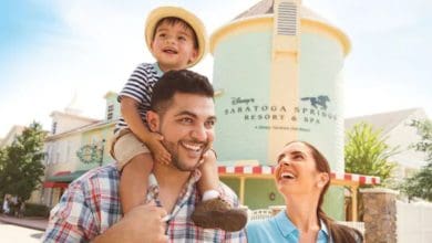Happy family outside Disney’s Saratoga Springs Resort & Spa, child riding on dad’s shoulders, enjoying the excitement and special experiences that come with a Disney resort stay.